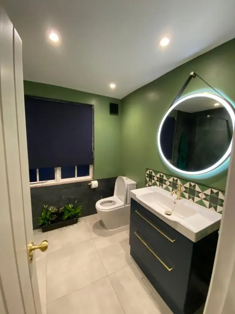 Refurbished bathroom with green walls, patterned tiles and a round lit mirror