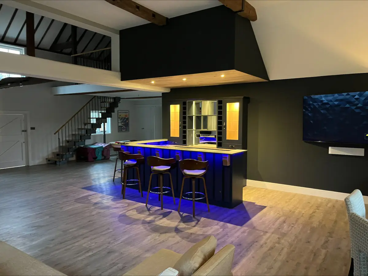 Open-plan room with exposed beams, a lit bar and a staircase to a mezzanine
